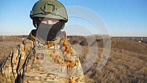Portrait of ukrainian army woman in helmet and balaclava at countryside. Female military medic looks into camera