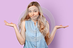 Portrait of uncertain young woman with blonde hair standing with raised arms  on color background