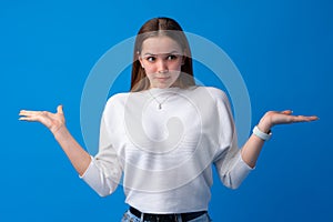 Portrait of uncertain young woman standing with raised arms on blue