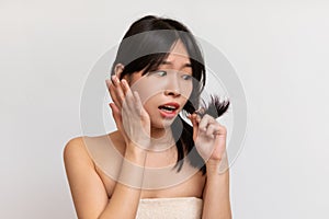 Portrait of unhappy Asian lady looking at her split ends