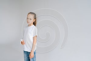 Portrait of unhappy blonde little girl with broken hand wrapped in white plaster bandage standing on light isolated