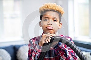 Portrait Of Unhappy Boy Reluctantly Helping Out With Chores At Home Holding Vacuum Cleaner