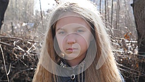 Portrait of unhappy child against the blurred background of a forest at early spring. Small disappointing girl looking