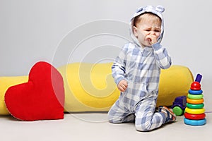 Portrait of unhappy little baby boy sitting with toys and crying.