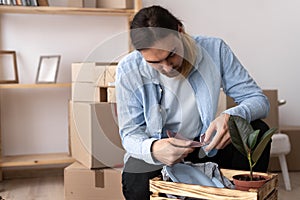 Portrait of unhappy modern man in t-shirt near cardboard box with a broken dish on home background