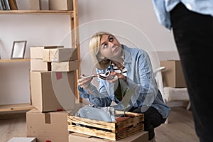 Portrait of unhappy modern woman in t-shirt near cardboard box with a broken dish