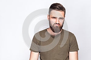 Portrait of unhappy sad bearded man with dark green t shirt against light gray background.