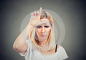 Portrait unhappy woman giving loser sign on forehead, looking at you with anger and hatred on face