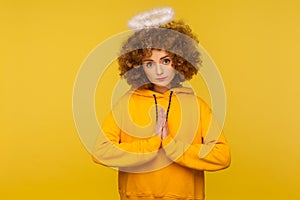 Portrait of unhappy woman with saint nimbus holding hands in prayer and looking with obedient expression