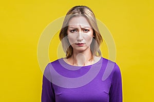 Portrait of unhappy young woman frowning and worrying about failure. indoor studio shot isolated on yellow background