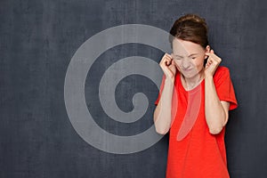 Portrait of unhappy young woman plugging her ears with fingers