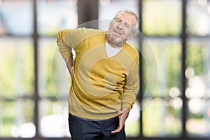 Portrait of unhealthy old senior man with bottom back pain.