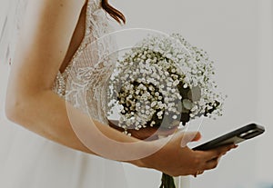 Portrait of an unrecognizable Caucasian bride with a bouquet of boutonnieres and a mobile phone.