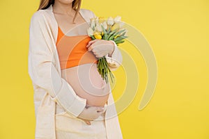 Portrait of unrecognizable pregnant woman wear orange top, beige cardigan, trousers, holding bunch of colorful tulips.