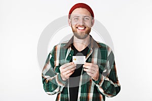 Portrait of unshaved man laughing and holding credit card, while standing isolated over white background