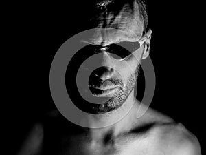 Portrait of unshaven adult caucasian man in swimming glasses. He looks straight to watcher. Black and white shot, low-key lighting