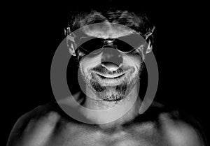 Portrait of unshaven adult caucasian man in swimming glasses. He smiles and looks straight to watcher. Black and white shot, low-