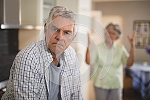 Portrait of unsmiling senior man with angry woman in background