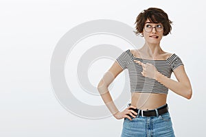 Portrait of unsure hesitating cute girlfriend in round glasses and striped cropped top, biting lip while thinking or