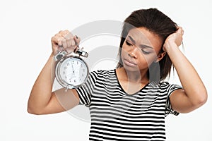 Portrait of an upset african girl looking at alarm clock