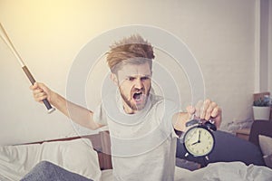 Portrait upset angry with baseball hit young man screaming at alarm clock on bedroom.