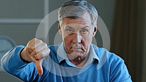 Portrait of upset angry sad elderly man looking at camera disgruntled serious mature old grandpa showing dislike thumbs