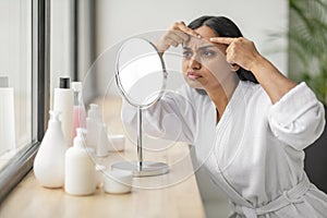 Portrait of upset beautiful young indian woman looking at mirror