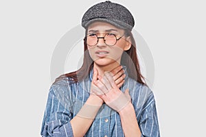 Portrait of upset brunette girl having cold or flu, feeling bad, standing against gray background. Young woman having a sore