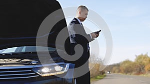 Portrait of upset businessman staying on countryside road, using smartphone for calling help evacuator evacuating repair