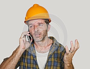 Portrait of upset construction worker or stressed contractor man in builder hat talking on mobile phone unhappy in stress messing