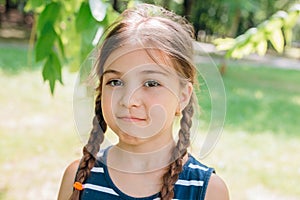 Portrait of an upset cute little girl with pigtails standing and looking at camera in summer