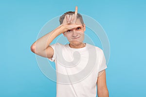 Portrait of upset depressed man in white t-shirt showing L sign on forehead, gesturing I`m loser