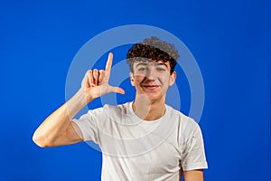 Portrait of upset depressed man in white t-shirt showing L sign on forehead, gesturing I'm loser, feeling defeated and