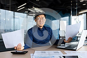 Portrait upset and disappointed Asian man, financier accountant doing paperwork looking at camera holding documents and