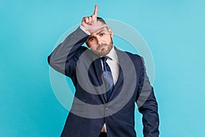 Portrait of upset disappointed young adult businessman with beard in dark suit standing, showing looser gesture with hand on