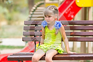 Portrait of upset five year old girl who is sitting on the bench on the background of the playground