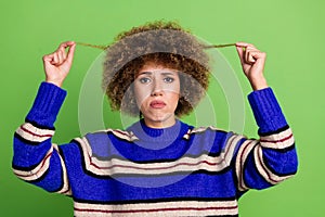 Portrait of upset girl with perming coiffure dressed knit pullover holding curls dislike hairdo isolated on green color