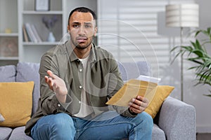 Portrait of an upset Latin American man who looks sadly into the camera and holds a letter with documents that he