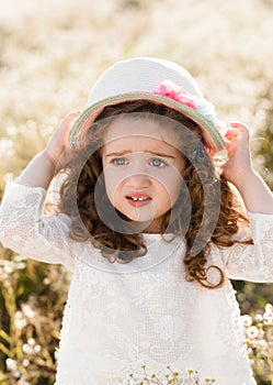 Portrait of an upset little girl in a straw hat with curly hair