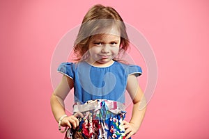 Portrait of upset little girl three years on pink isolated background, expresses frustration or resentment, demonstrates