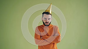 Portrait of upset man in party hat standing alone with arms crossed sighing