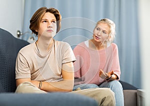 Upset and offended teenager sitting on sofa while mother soothing him