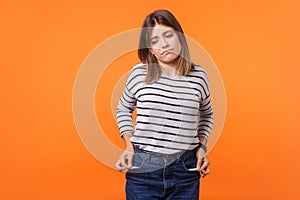 Portrait of upset poor young woman with brown hair in long sleeve striped shirt. indoor studio shot isolated on orange background