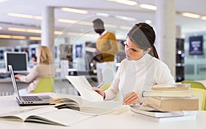 Portrait of upset tired female student preparing for exam in university library