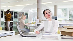 Portrait of upset tired female student preparing for exam in university library