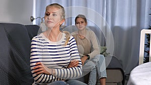 Portrait of upset woman sitting on sofa at kitchen after quarrel, her teenage daughter trying conversate with her