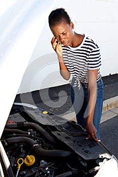 Upset young african woman standing by broken down car parked on the side of a road and calling for assistance