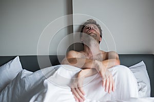 Portrait of an upset young man sitting on a bed alone.