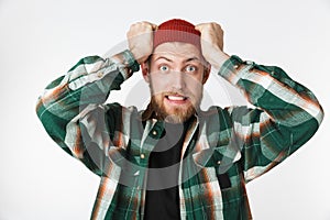 Portrait of uptight man wearing hat and plaid shirt screaming and grabbing head, while standing isolated over white background