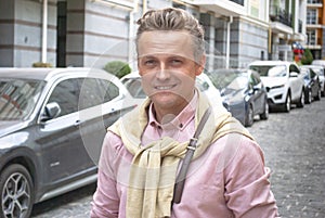 portrait of urban mature attractive man with bag walking on city street with parked cars